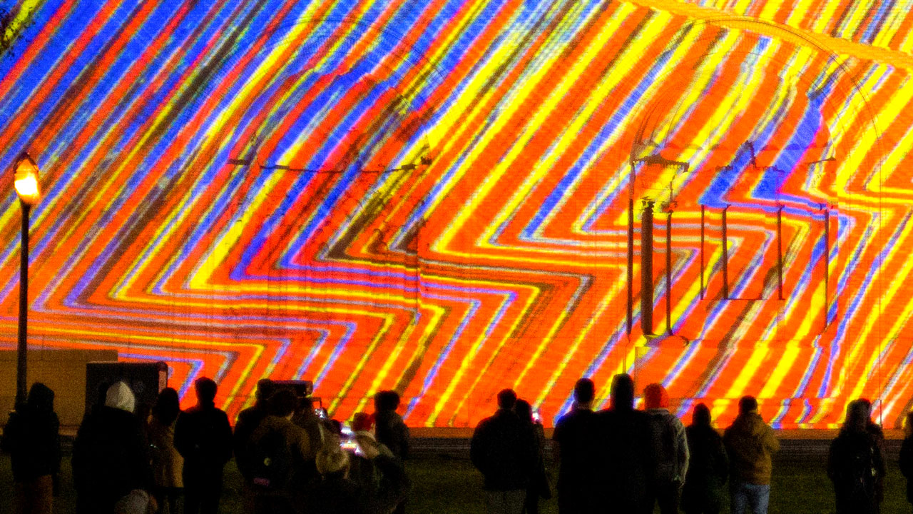 Bright, multicolored light projected in a wavy pattern upon a building wall.